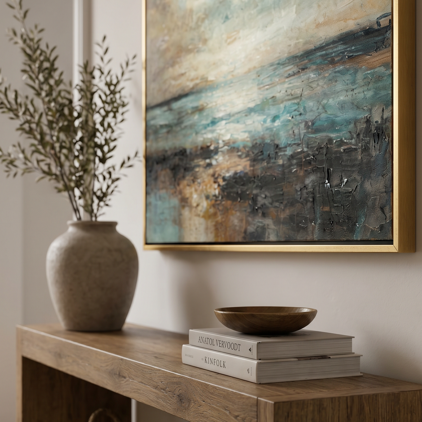 Decorative setup with a vase, books, and a bowl on a wooden console table, featuring an abstract painting in the background.